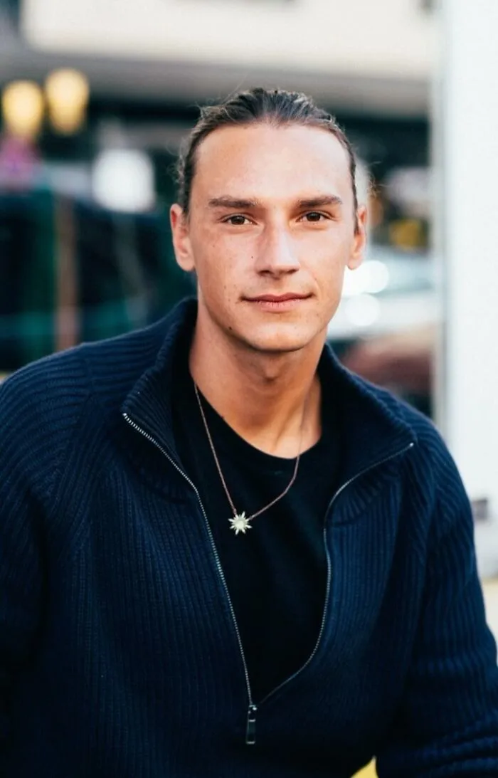 A visually striking street portrait of a stranger with long hair, wearing a dark sweater and star necklace.