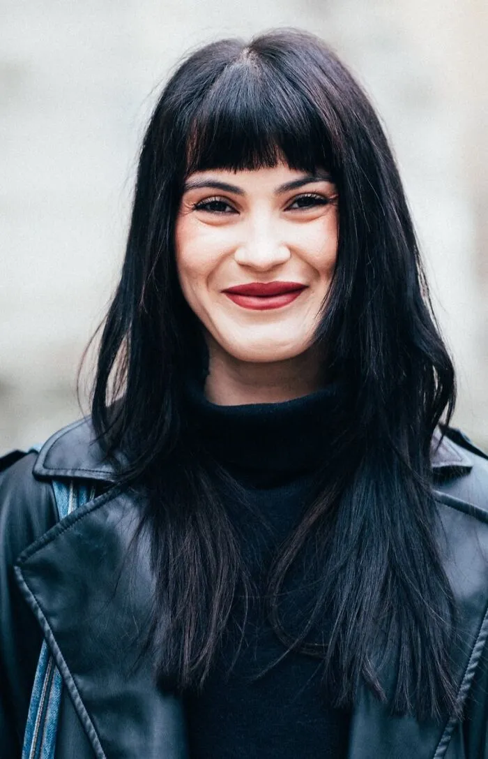 Striking street portrait of a smiling woman with dark hair and leather jacket, showcasing urban photography.