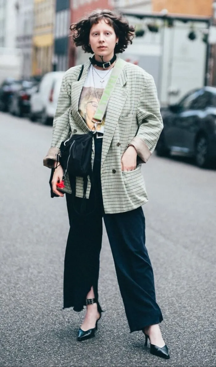 Street portrait of a stylish individual in a plaid jacket and black pants, standing confidently on an urban road.