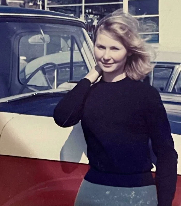 Young woman posing by a vintage car in a candid glimpse into the past, capturing an authentic moment of history.