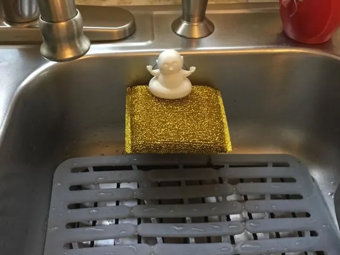 Duck-shaped soap holder on a golden sponge in a kitchen sink, by Peleg Design Shop.