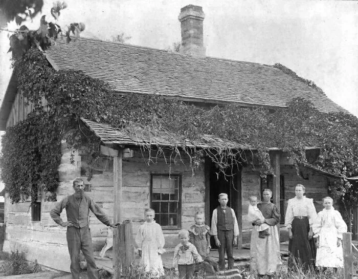 Black and white photo of a family standing outside a rustic house, offering a candid glimpse into the past.