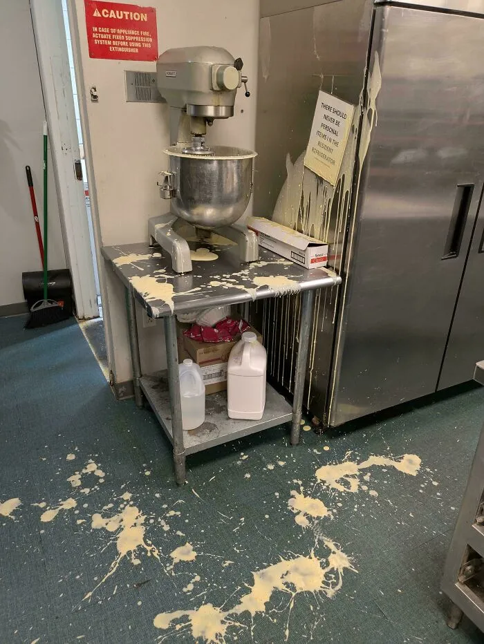 Batidora industrial derrama masa en cocina, mostrando un día difícil en el trabajo.