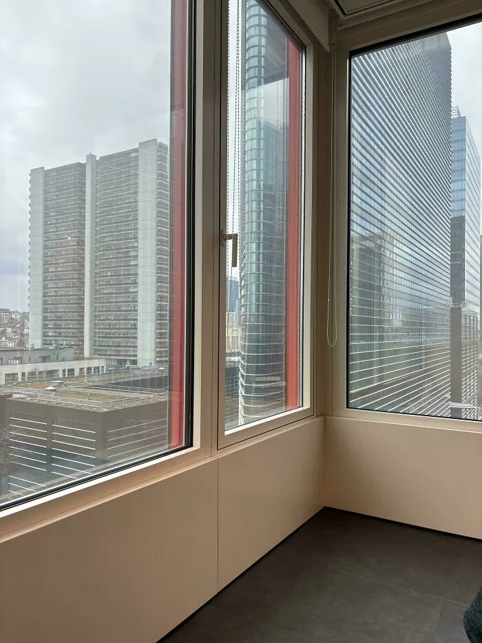View from inside an office corner overlooking tall buildings with windows demonstrating ignored safety protocol risks.