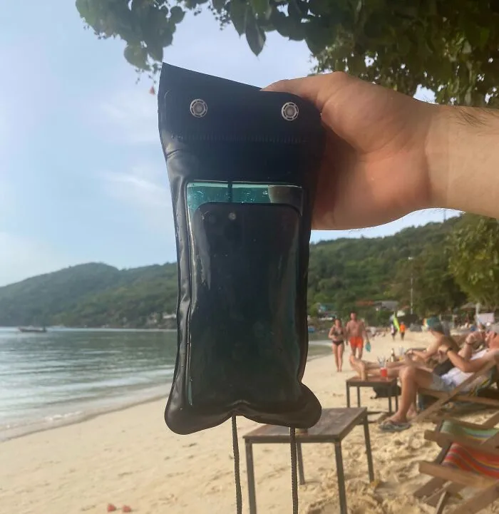 Teléfono mojado en funda impermeable junto al mar, ejemplo de accidente costoso en la playa.