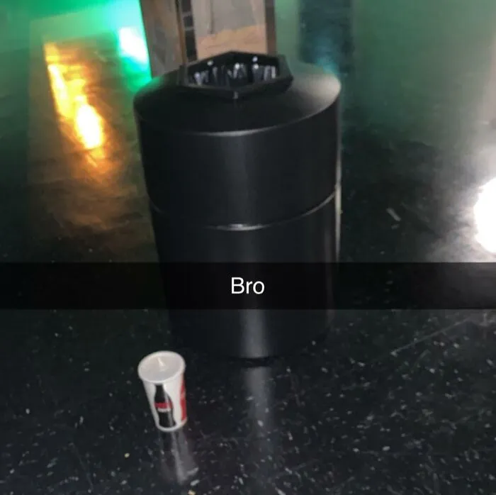 Basurero negro en interior con vaso de bebida en el suelo, ilustrando situaciones frustrantes con clientes según empleados.