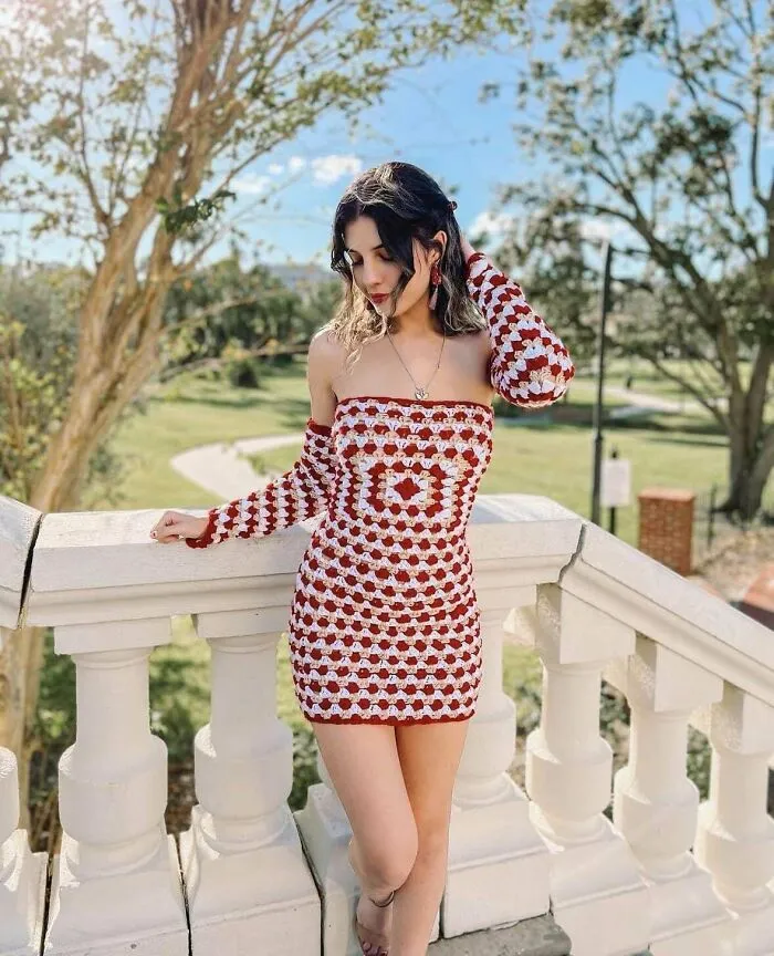 Woman wearing a handmade red and white crochet dress with matching sleeves, standing outdoors near a white stone railing.