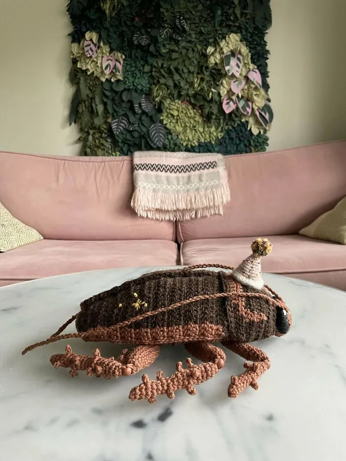 Crochet enthusiasts made an incredible realistic bug with detailed legs and a small party hat on a marble table.