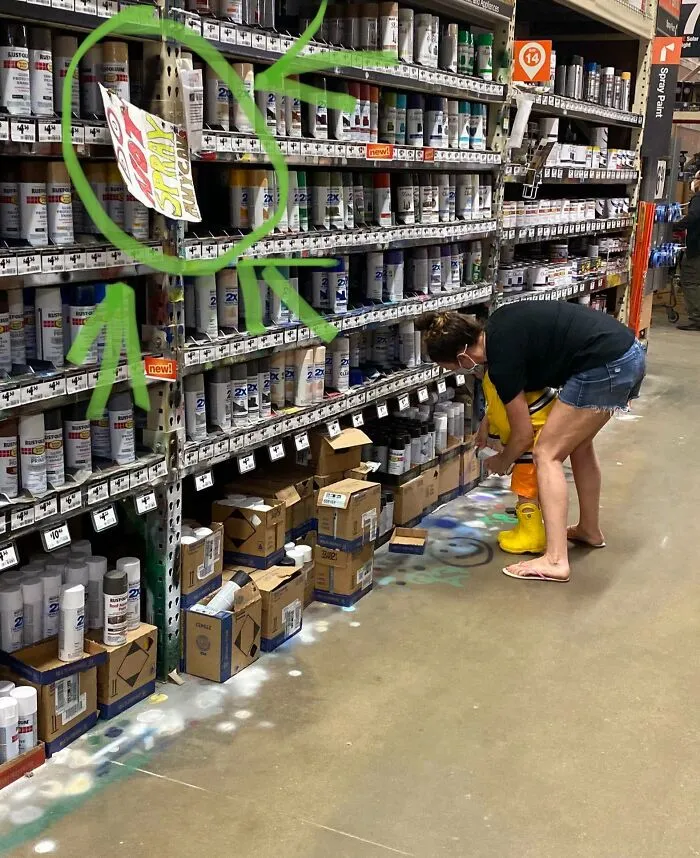Una madre enseña a su hijo a pintar con aerosol el suelo de la tienda. Justo al lado del cartel que pone no usar los aerosoles