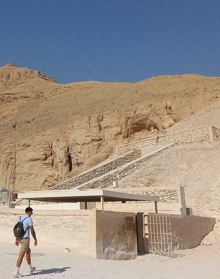 Un hombre caminando junto a una estructura en un sitio arqueológico bajo un cielo despejado.