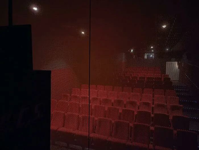 Sala de cine vacía vista a través de un panel perforado, lugar conocido con nueva perspectiva.