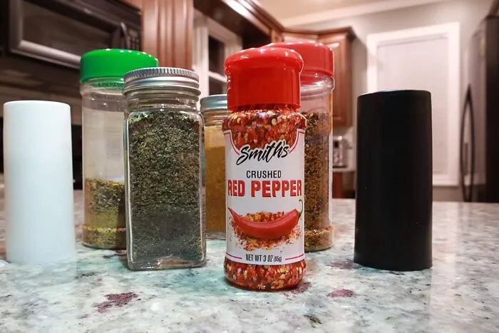 Crushed red pepper jar and spice containers on a kitchen counter for family-friendly April Fools pranks.