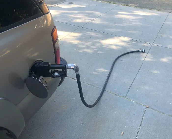 "Manguera de gasolina olvidada conectada a un coche estacionado, un error digno de compartirse en internet."