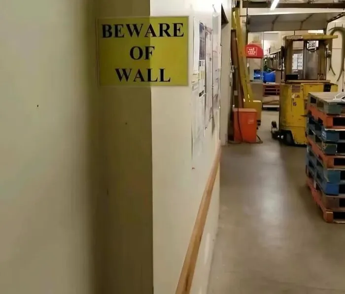 Aviso legal divertido en bodega industrial con señal de precaución sobre la pared para evitar accidentes laborales.