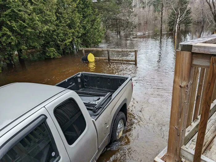 Camioneta atrapada en inundación cerca de árboles y barandilla, escena de personas teniendo un mal día.