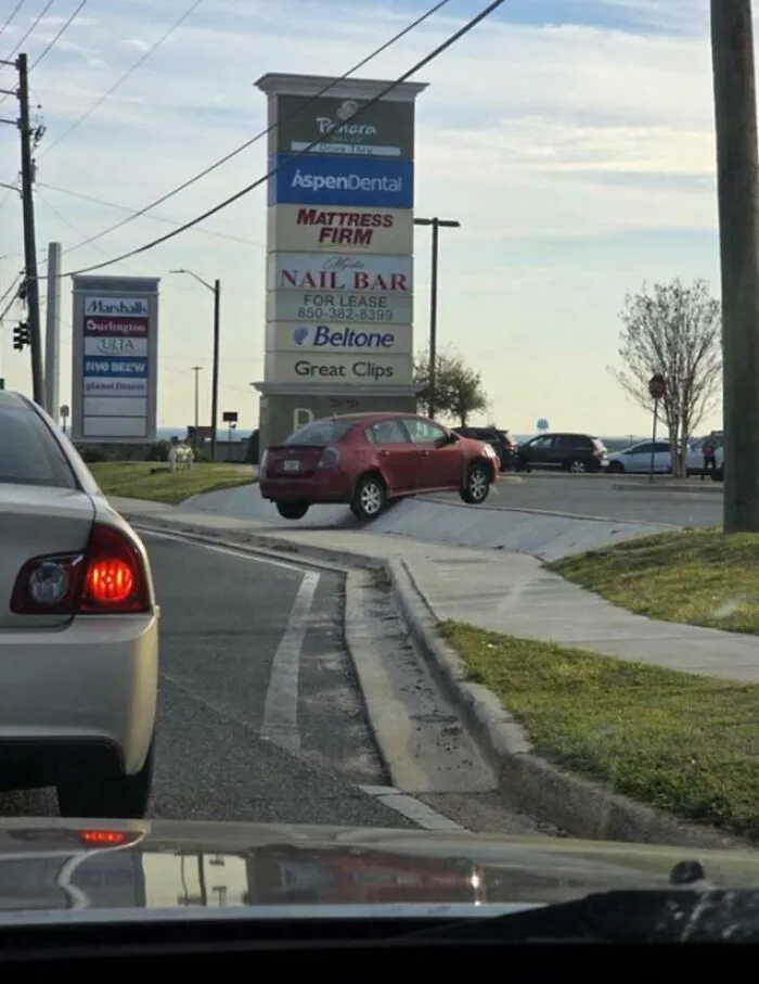 Coche rojo mal estacionado en una acera frente a una plaza comercial, ejemplo de errores compartidos en internet.