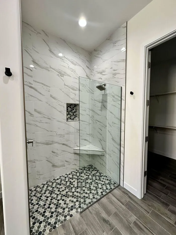Modern shower with glass doors, dark hexagonal floor tiles, and marble-patterned walls, showcasing interior design trends to avoid.