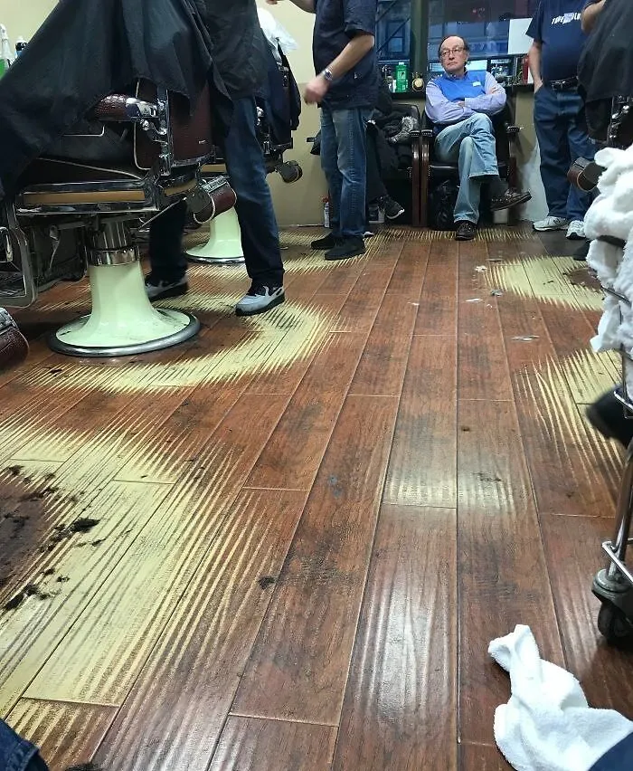 Barber shop floor showing wear patterns from time and use, with people seated and waiting.
