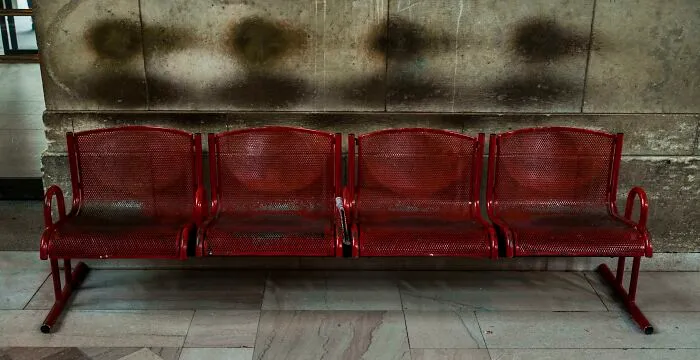 Aged red metal bench with wear marks on a wall, showing transformation by time and use.