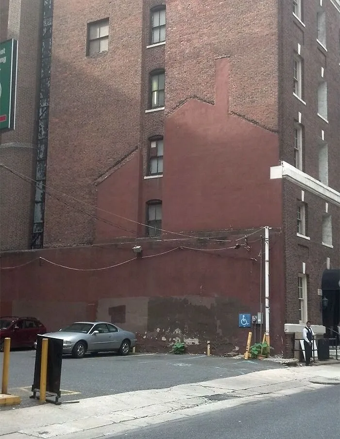 Unused parking area beside a brick building, showing the faded outline of a removed building, transformed by time and use.