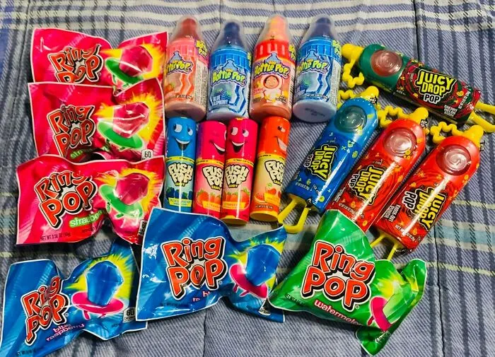 Colorful Easter basket stuffers featuring Ring Pops and candy drinks on a striped cloth background.