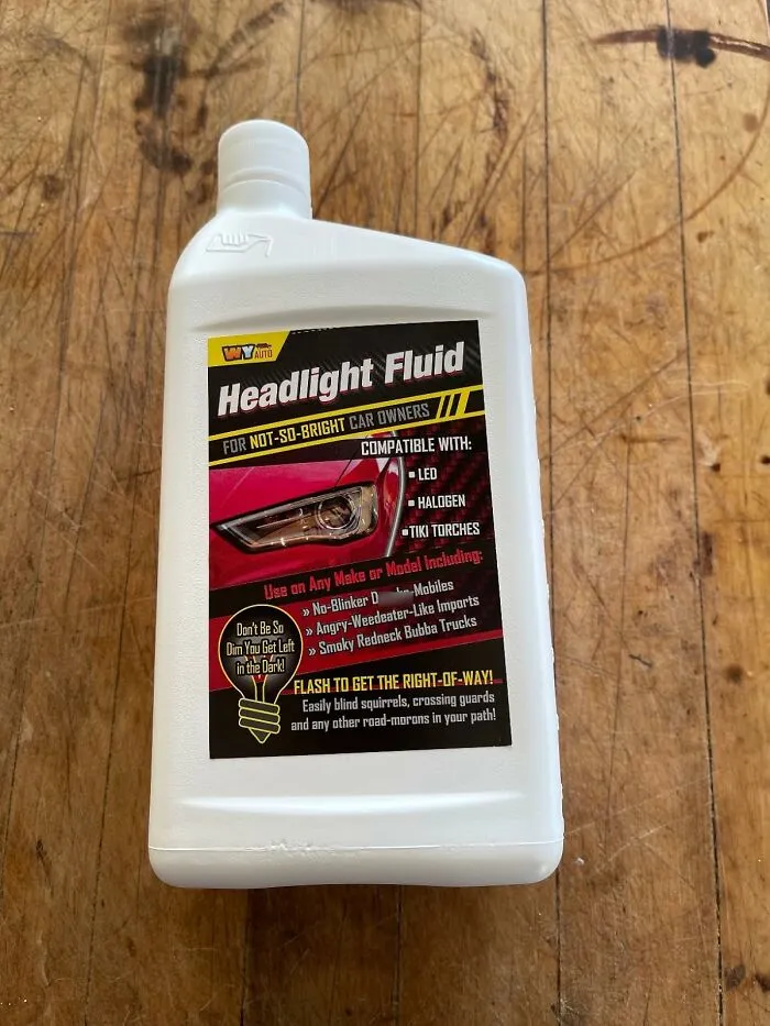 Bottle of humorous "Headlight Fluid" on a wooden table, featuring playful April Fools prank details on label.