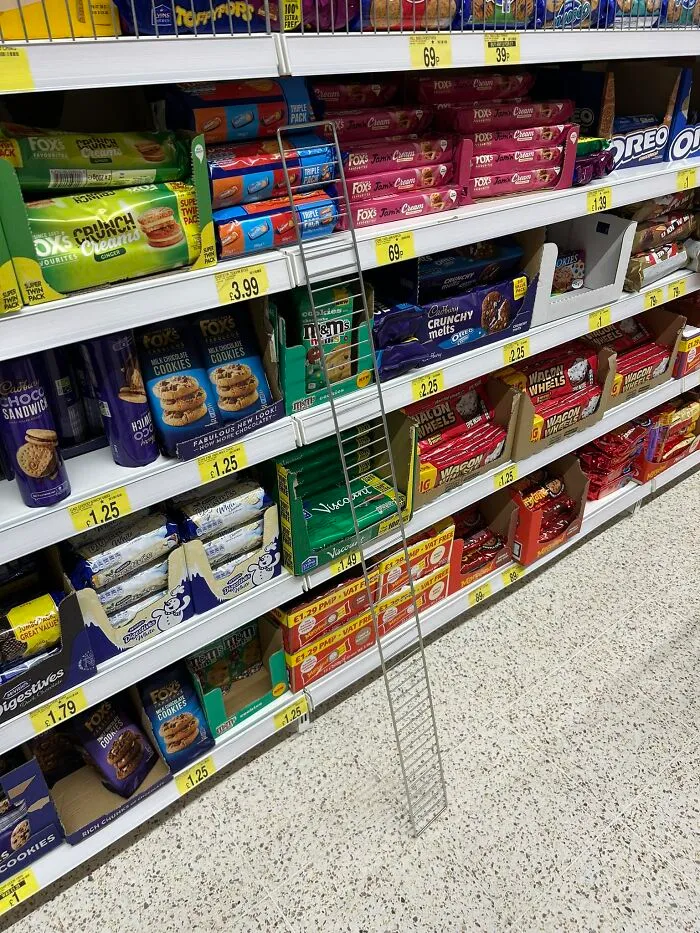 A wire shelf frame leaning against a British supermarket aisle displaying various biscuits and snacks.