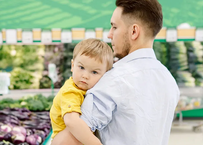 A man carries a child through a grocery store, highlighting parenting behaviors.