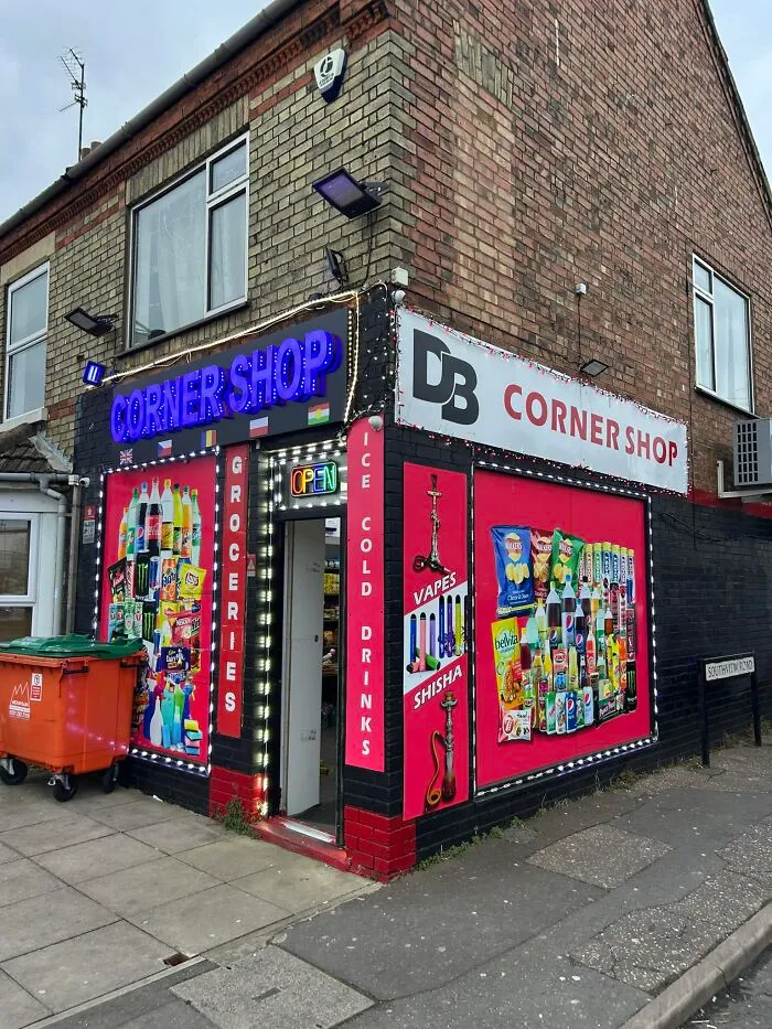 Corner shop in the UK with colorful window displays featuring groceries and drinks, iconic British setting.