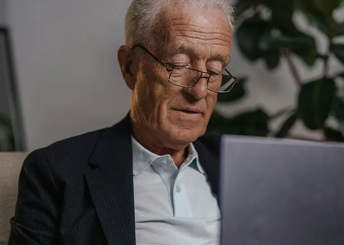 Elderly man using a laptop, reflecting on life without social media, wearing glasses and a suit jacket.