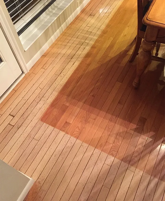 Worn wooden floor showing color contrast, transformed by time and use, near a window and table.