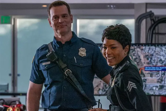 TV couple in uniform smiling, standing in an office setting.