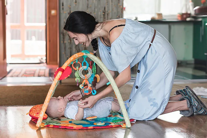 Woman playing with a baby on a colorful play mat in a cozy home setting, highlighting normal USA parenting activities.