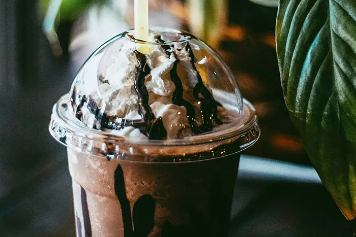 Milkshake with whipped cream and chocolate drizzle in a plastic cup, highlighting American food culture.