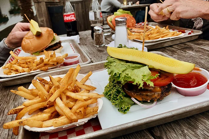 American burgers and fries on a wooden table, with sodas and condiments, showcasing typical USA dining.