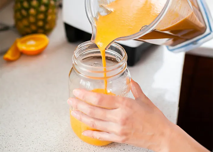 A person pouring an orange smoothie from a blender into a jar, illustrating a diet-related concept.