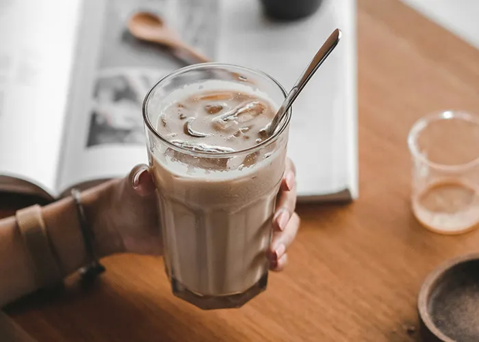 Hand holding iced coffee next to an open book, representing worst diets concept.