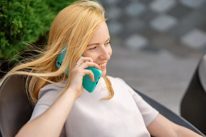 Person smiling while talking on a turquoise phone, representing gradually disappeared habits.