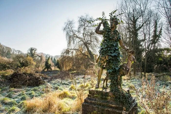 Abandoned statue overgrown with ivy in a deserted, eerie landscape.
