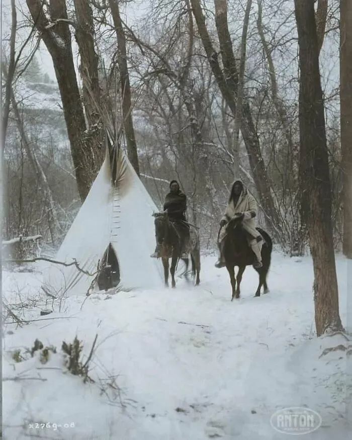 Dos nativos americanos apsaroke a caballo fuera de un tipi en un bosque nevado de Montana en 1908