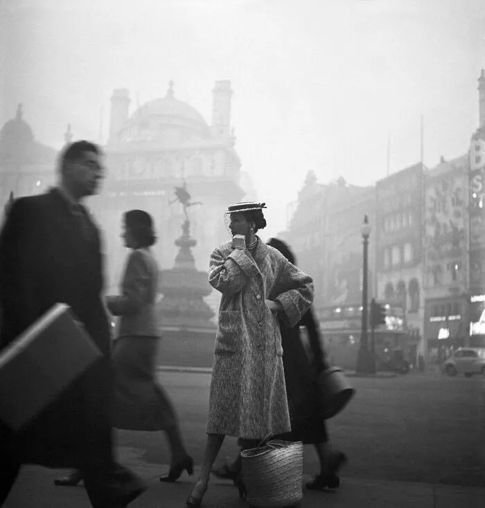 Vintage street scene with a stylish woman in a coat and hat, evoking historical nostalgia in a foggy city setting.