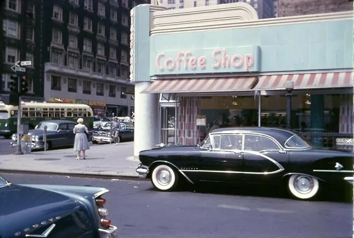 Vintage cars parked outside a classic coffee shop, evoking nostalgia in a bustling city scene.