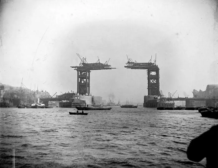Historical construction of a bridge over a river, boats in foreground, capturing nostalgia in black and white photography.