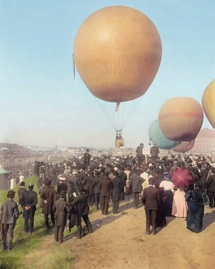 Historical pic of a crowd watching hot air balloons taking off, evoking nostalgia with vintage fashion and scenery.