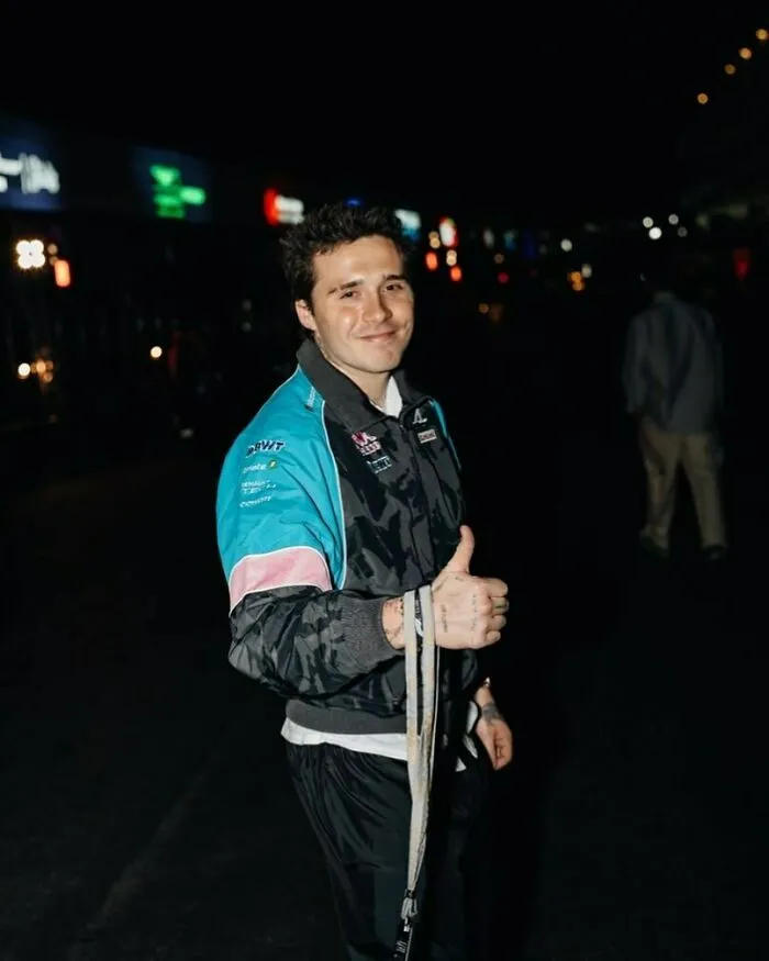 Person in a sporty jacket gives a thumbs-up at a night event, representing not-self-made-celebs theme.