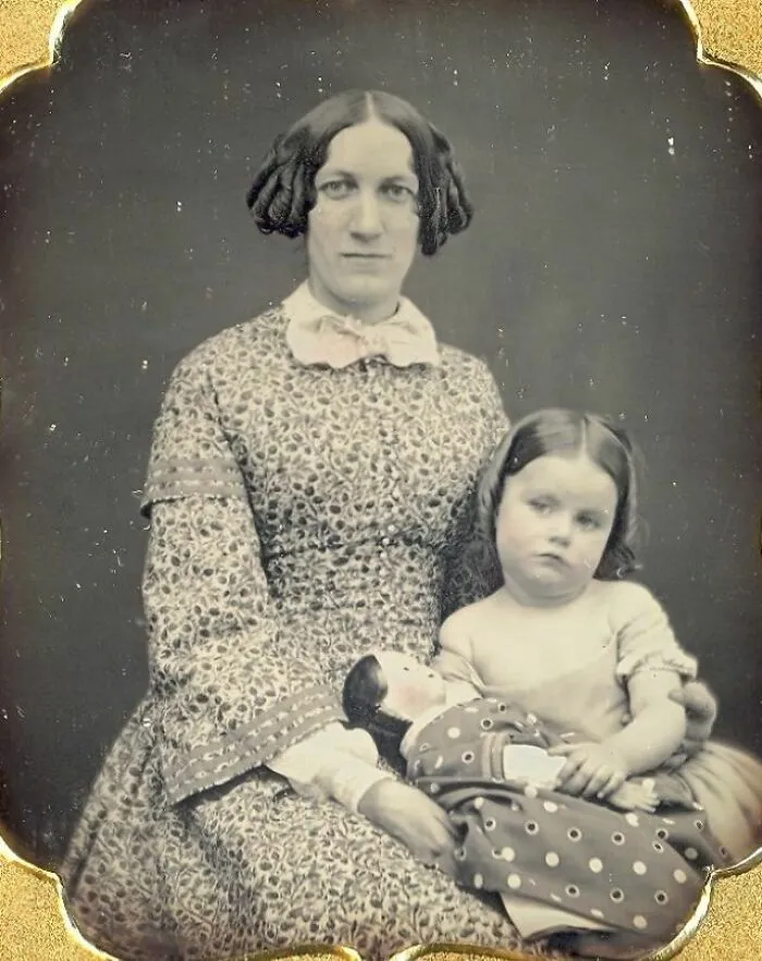 Historical photo of a woman and child in 19th-century attire, the child holding a doll.