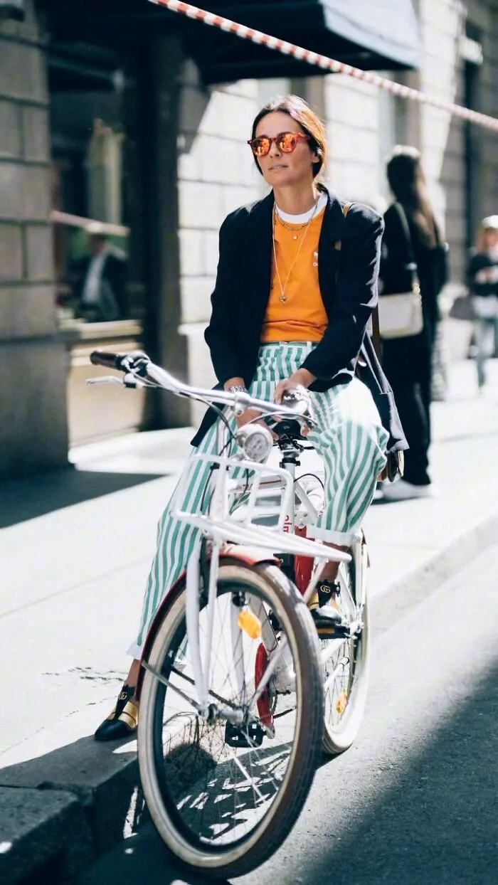 Woman in sunglasses riding a bicycle on a city street, showcasing street portraits style photography.