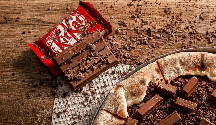 Chocolate pizza with KitKat pieces on top, resting on a wooden table, illustrating a dessert debate.