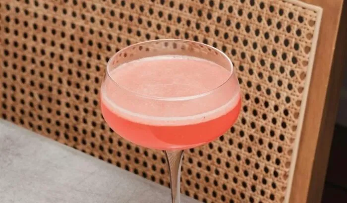 A pink cocktail on a table with a woven chair backdrop, highlighting evening relaxation benefits.