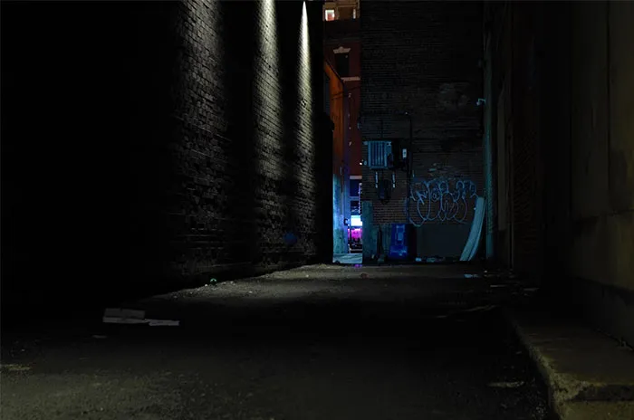 Dark urban alleyway at night, dimly lit, suggesting a creepy atmosphere.